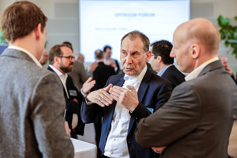 Three men in suits talking to each other at ZETA Symposium